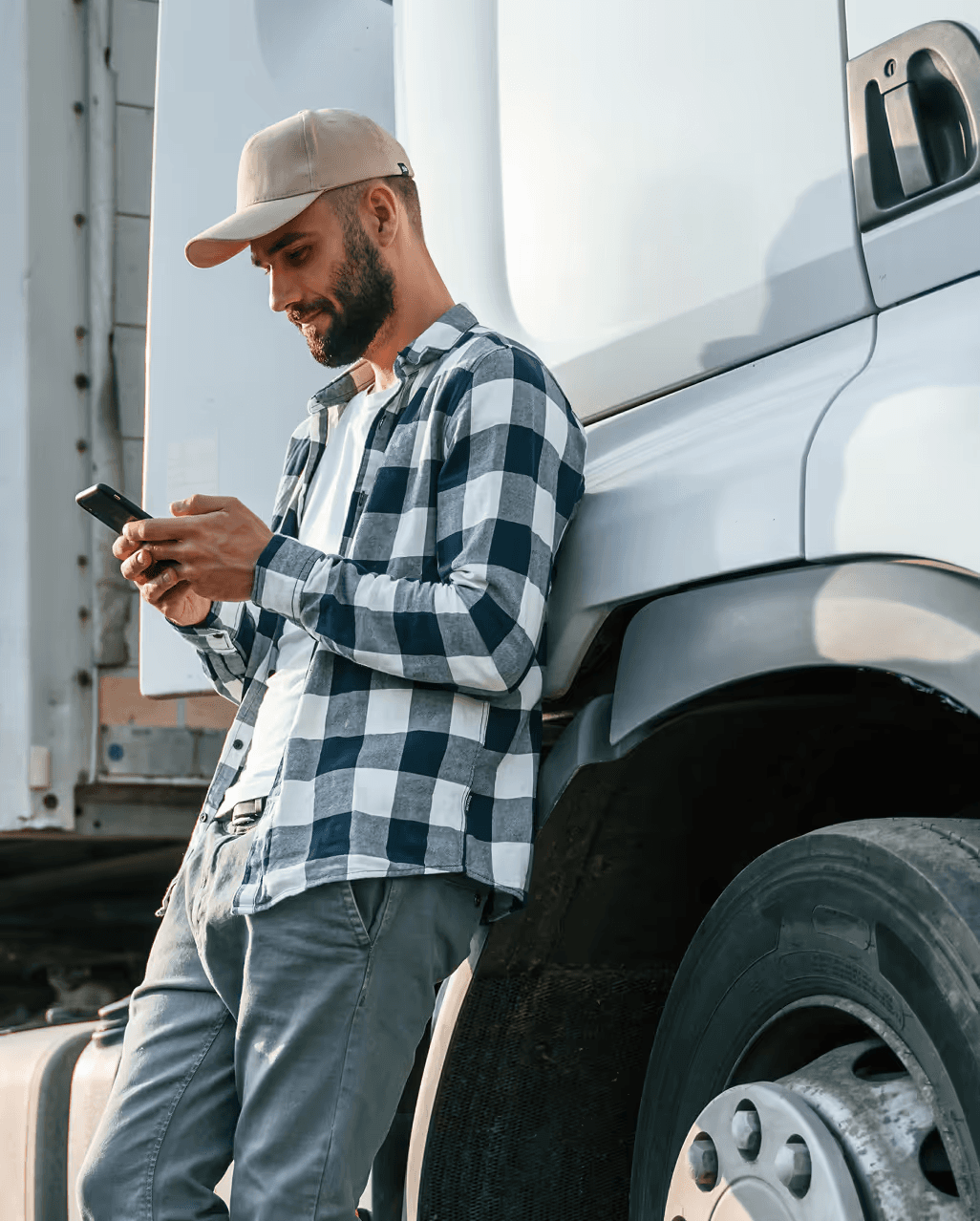 A delivery driver checking a dispatch on his phone beside his truck